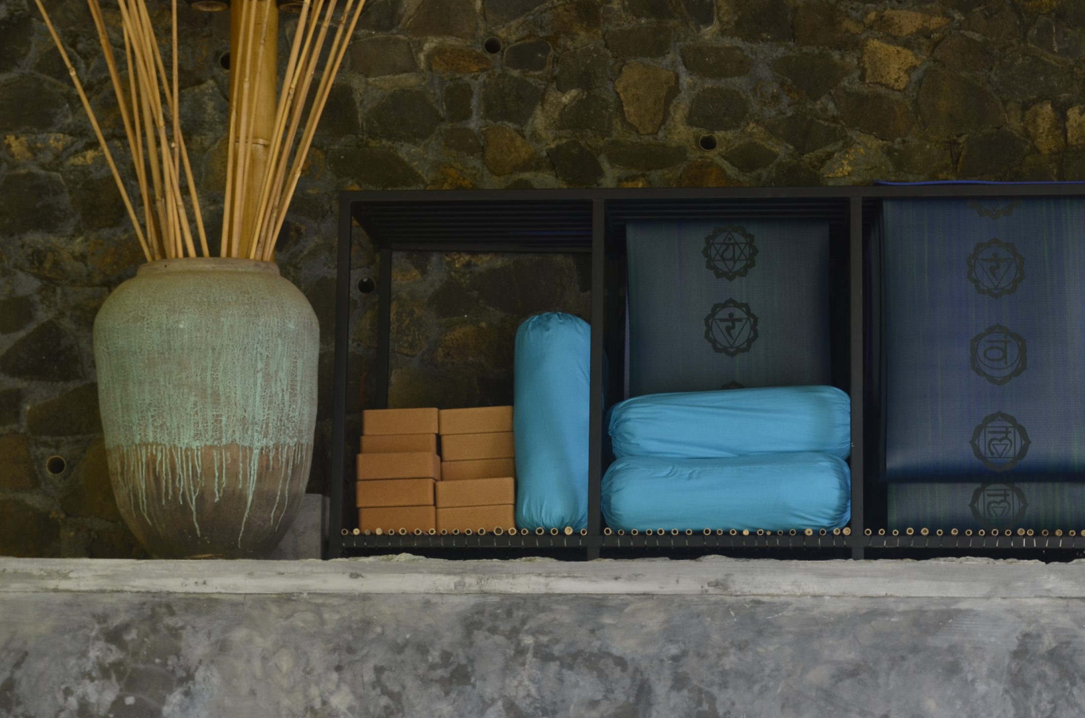 Folded blankets, blocks and yoga props stacked in a stone niche at Alamanda